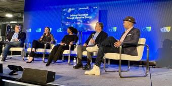 Image of a panel discussion - five people sit on stage holding microphones