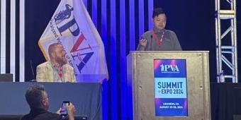 Photograph of Michael Huang speaking at the podium with a PVA flag behind him