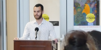 Mitch Bell speaks at a podium in front of a large crowd during the opening of the Assist+ center